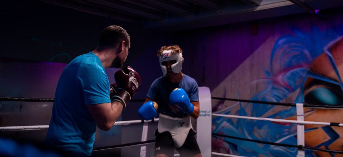 Two male boxers engaged in training in an indoor boxing ring with colorful graffiti.
